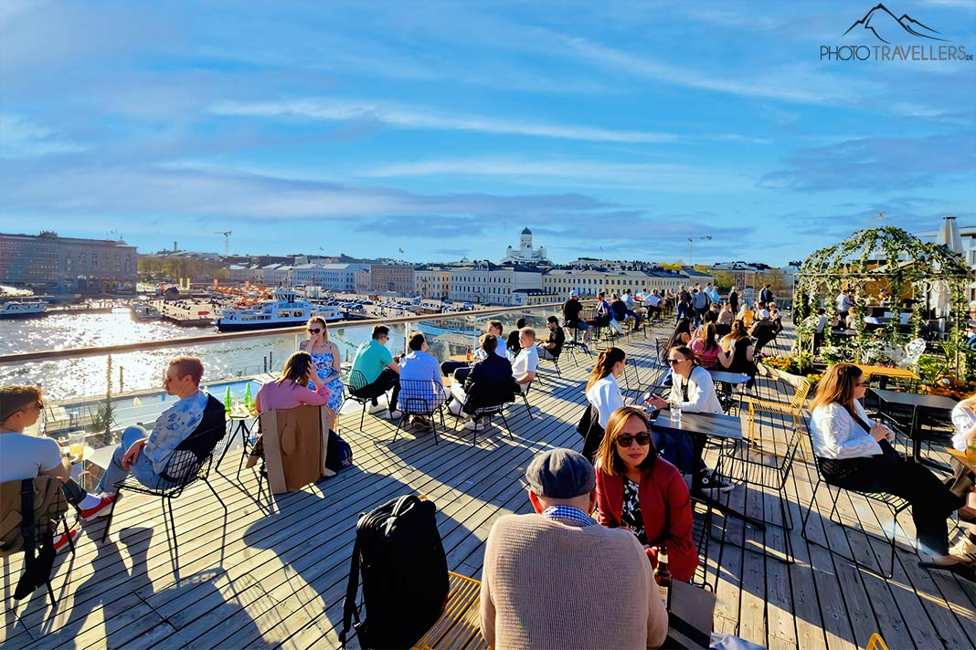 Menschen sitzen auf der Terrasse einer Bar im Hafen von Helsinki