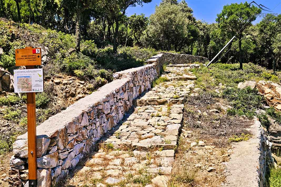Eine kleine Wandertafel am Rande eines gepflasterten Steinpfads am Berg Palouki