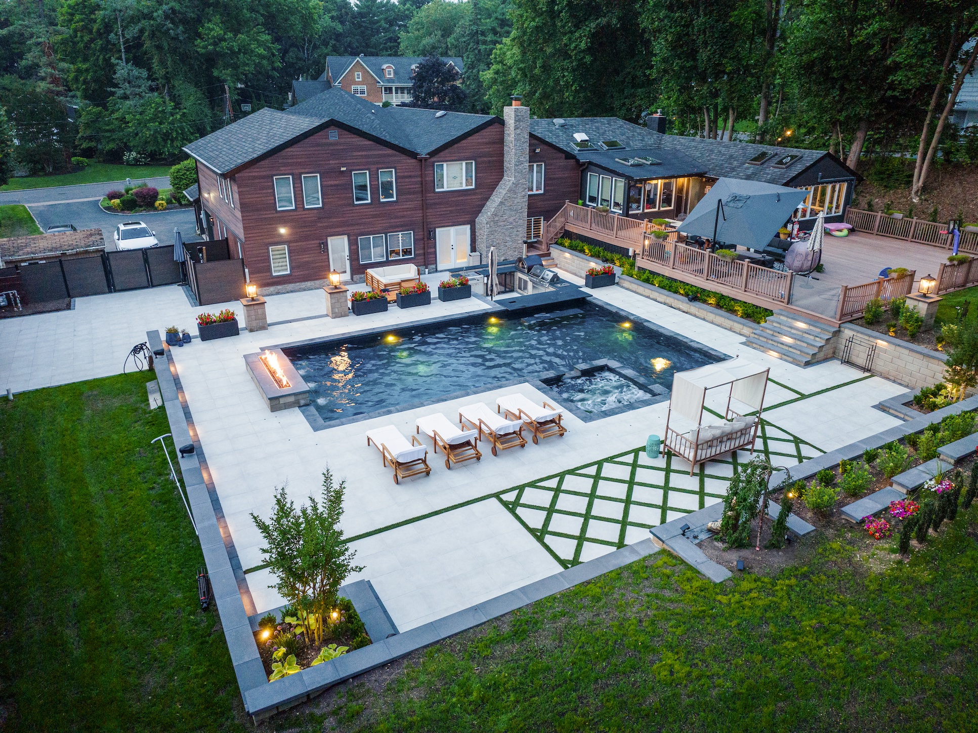 Aerial view of a modern backyard with a pool, lounge chairs, seating areas, and landscaped greenery next to a large two-story house.