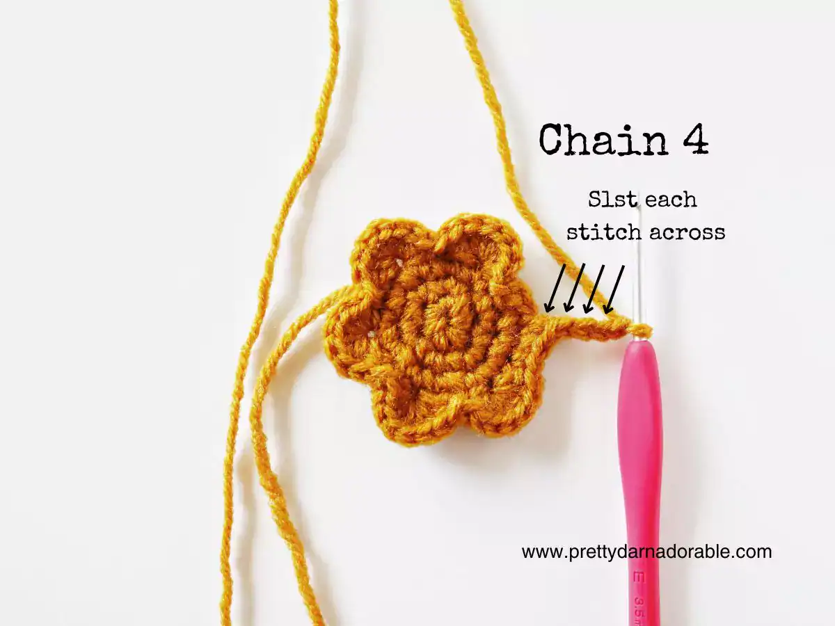 Yellow crocheted flower with pink hook in a stitch, text: “Chain 4, Slst each stitch across,” arrows highlight stitches; site at bottom. Free crochet pattern