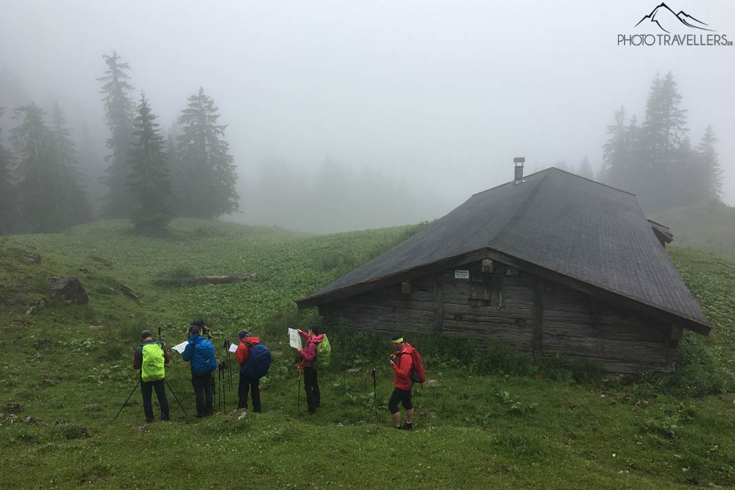 Fünf Teilnehmer der Wanderleiter-Ausbildung mit Karten vor einer Berghütte im Nebel