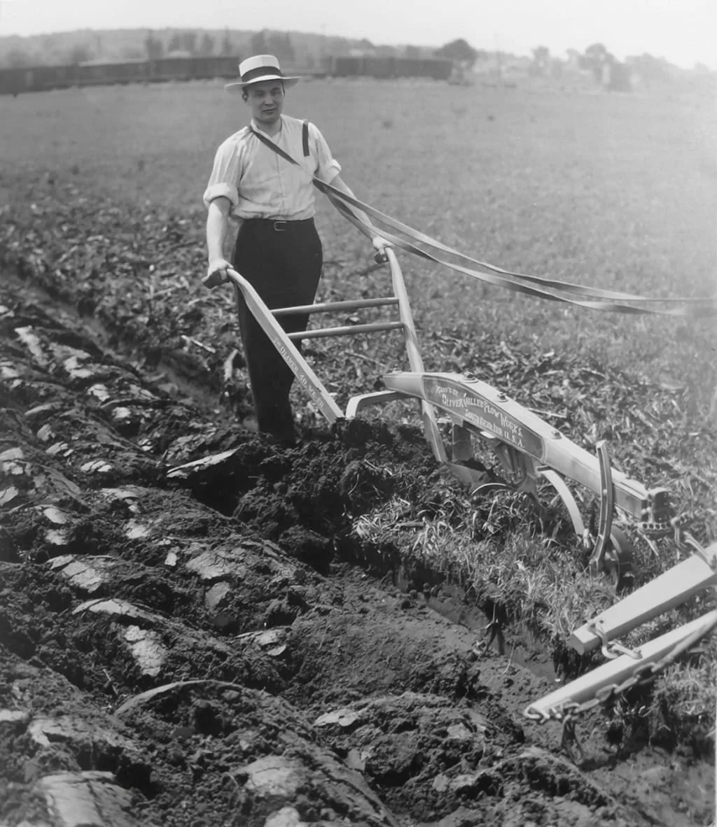 JD Oliver Jr_Plowing Vintage black and white photo of a man using a potato planter in a field, showcasing early agricultural technology and farming history.
