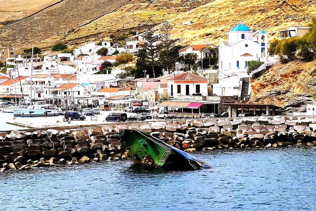 Die grüne Bugspitze eines Schiffswracks ragt vor der Kaimauer von Korissia aus dem Wasser