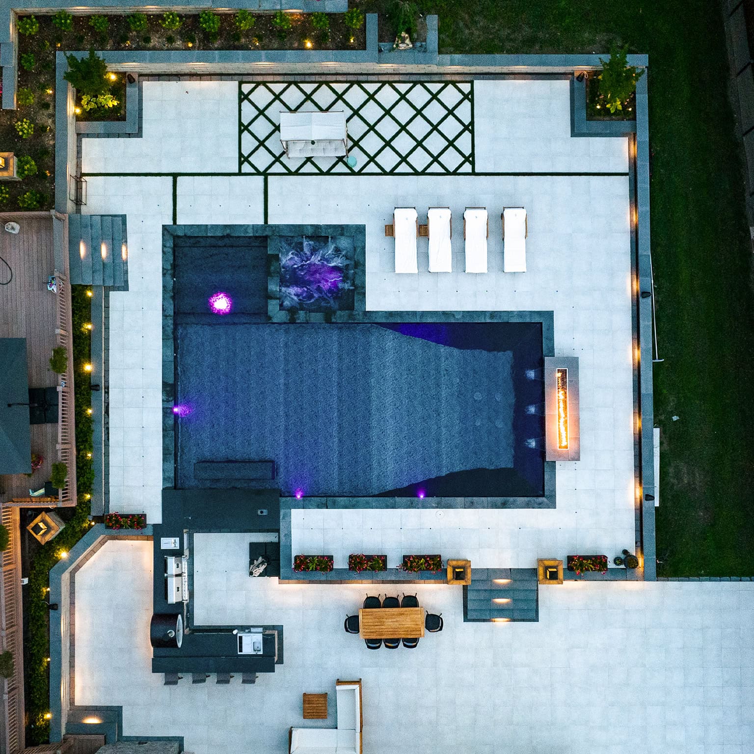 Aerial view of a modern backyard featuring a new gunite pool, lounge chairs, dining area, outdoor kitchen, and a landscaped patio with geometric patterns.