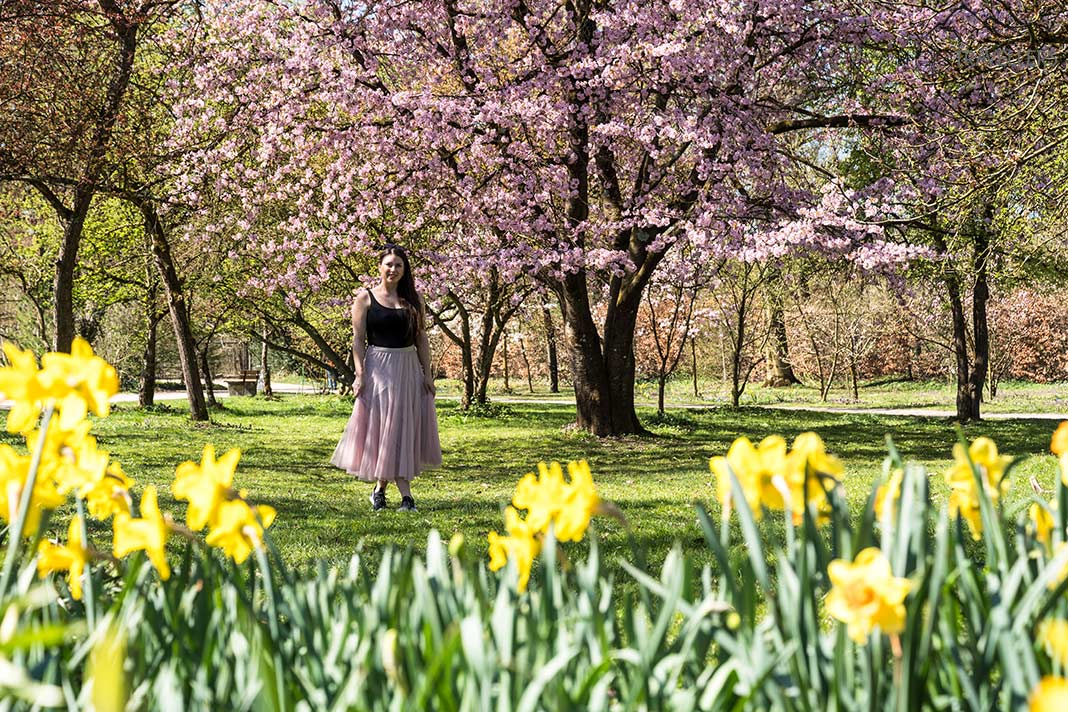 Reisebloggerin Biggi Bauer vor einem rosa blühenden Kirschbaum im Rosengarten, München