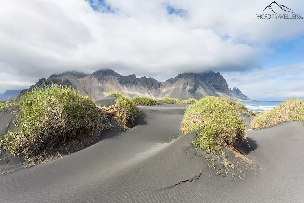 Schwarzer Sand und mit Gras bewachsene Hügel auf der Landzunge Stokksnes, im Hintergrund Berge