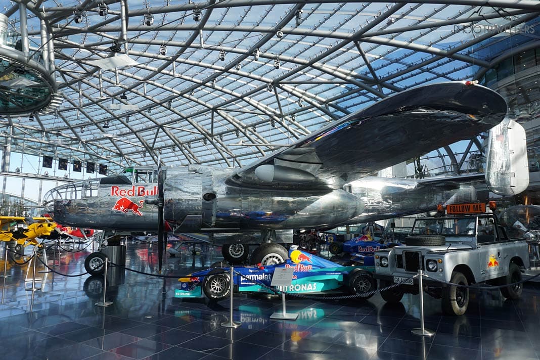 Ein Flugzeug vom Typ Douglas DC-6 mit "Red Bull"-Aufschrift hinter einem Formel-1-Auto und einem Landrover im Hangar 7 in Salzburg