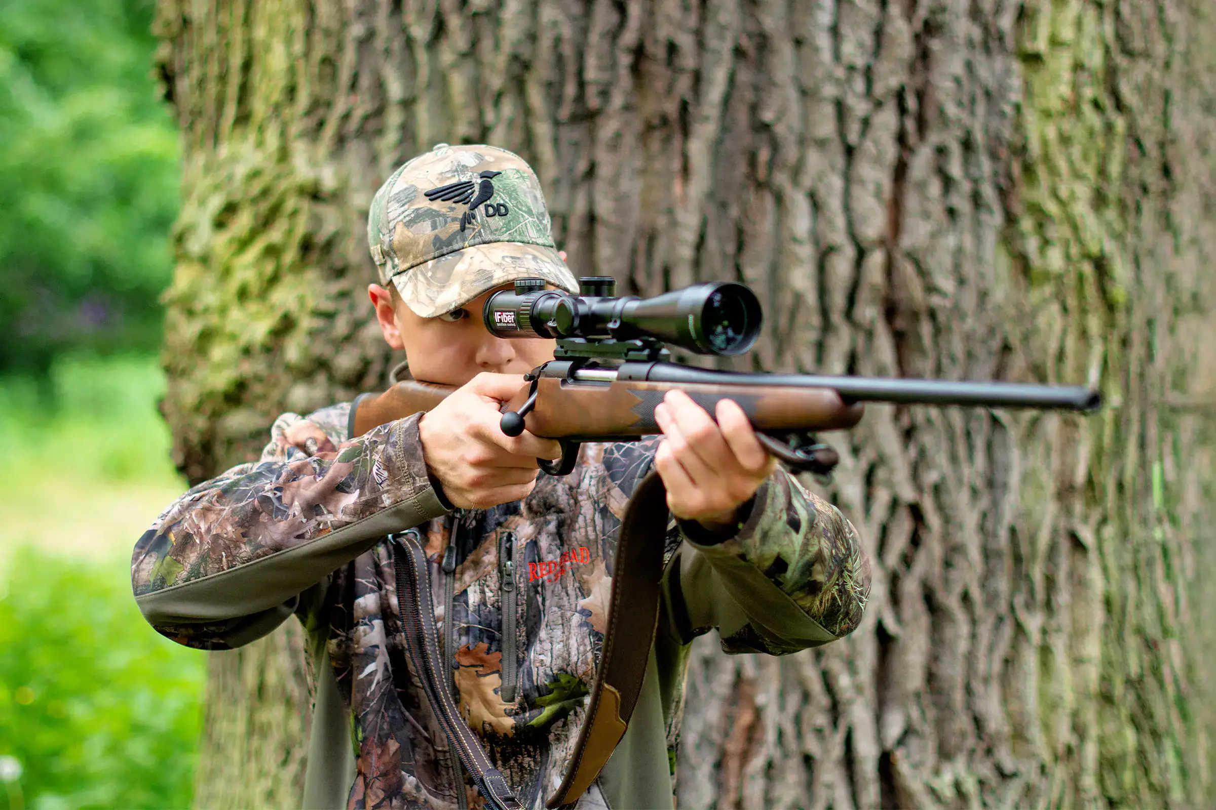 Jäger mit Jagdgewehr im Anschlag im Wald – optimales Setup für Sau, Reh, Hirsch und Fuchs