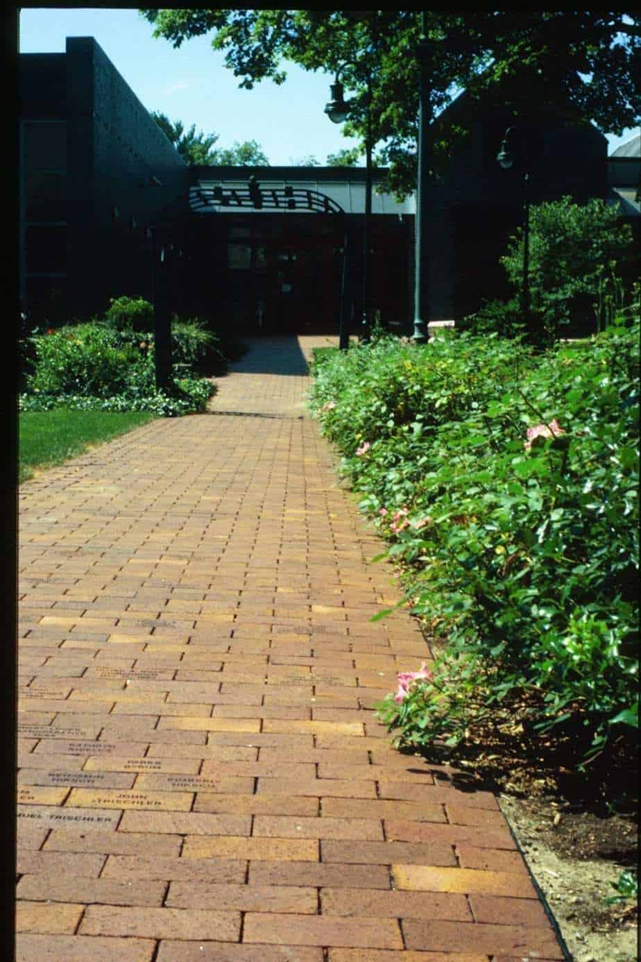 walkway Red brick pathway leading to The History Museum with surrounding lush garden greenery and blooming flowers.