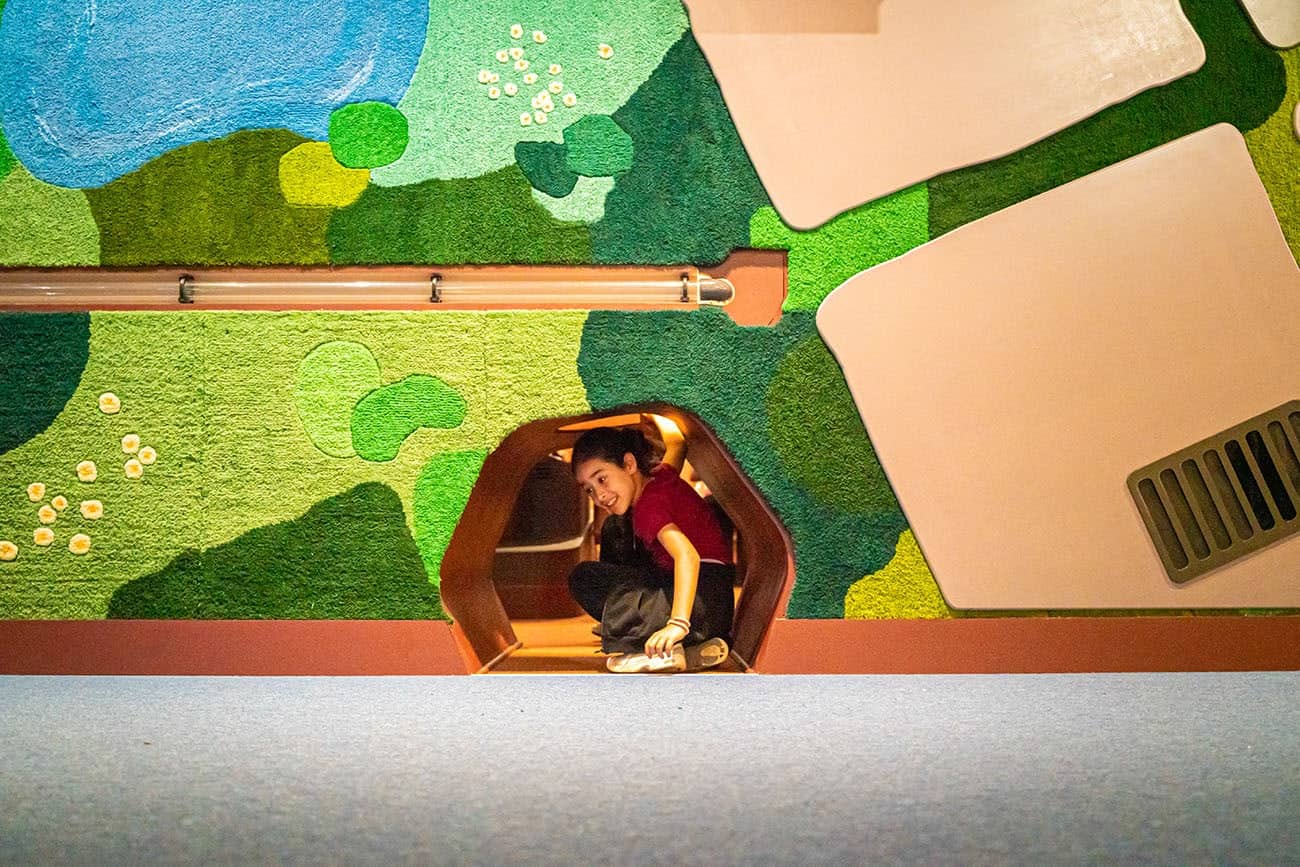 TEXTE ALT: Enfant souriant dans une pièce d'arcade ou salle d'activités avec un mur mural coloré représentant un paysage de nature.