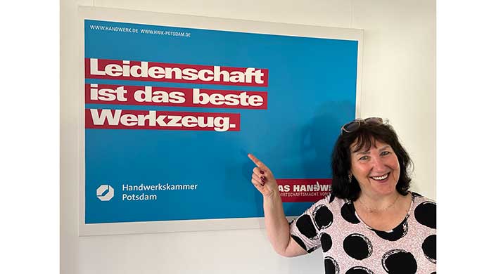 Eine Person zeigt auf ein blaues Plakat mit weiß-rotem Text. Nur der Arm der Person ist zu sehen.