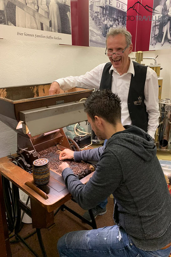 Reisejournalist Florian Westermann sitzt am Kaffeesortierer in der Kaffeerösterei Krimse, der Chef der Rösterei, Jens Kirmse, schaut dabei zu