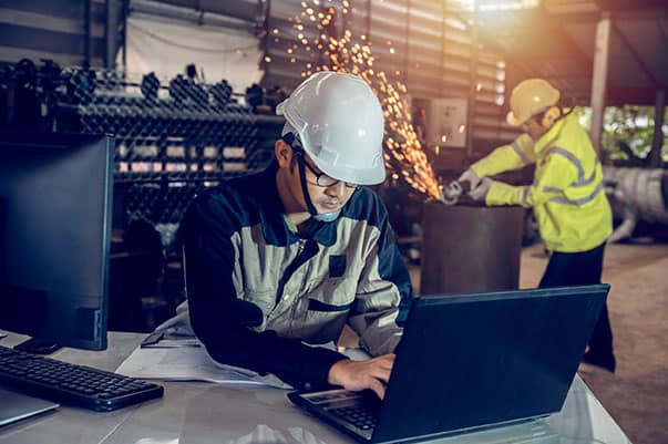 製造業移工申請專案 工廠工程師在零件作業中使用筆記型電腦,專注於生產流程控制。.