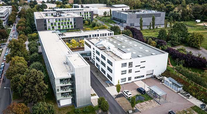 Mehrere moderne Bürogebäude mit flachem Dach, weißen Fassaden und großen Fenstern in einer grünen Landschaft aus der Vogelperspektive.