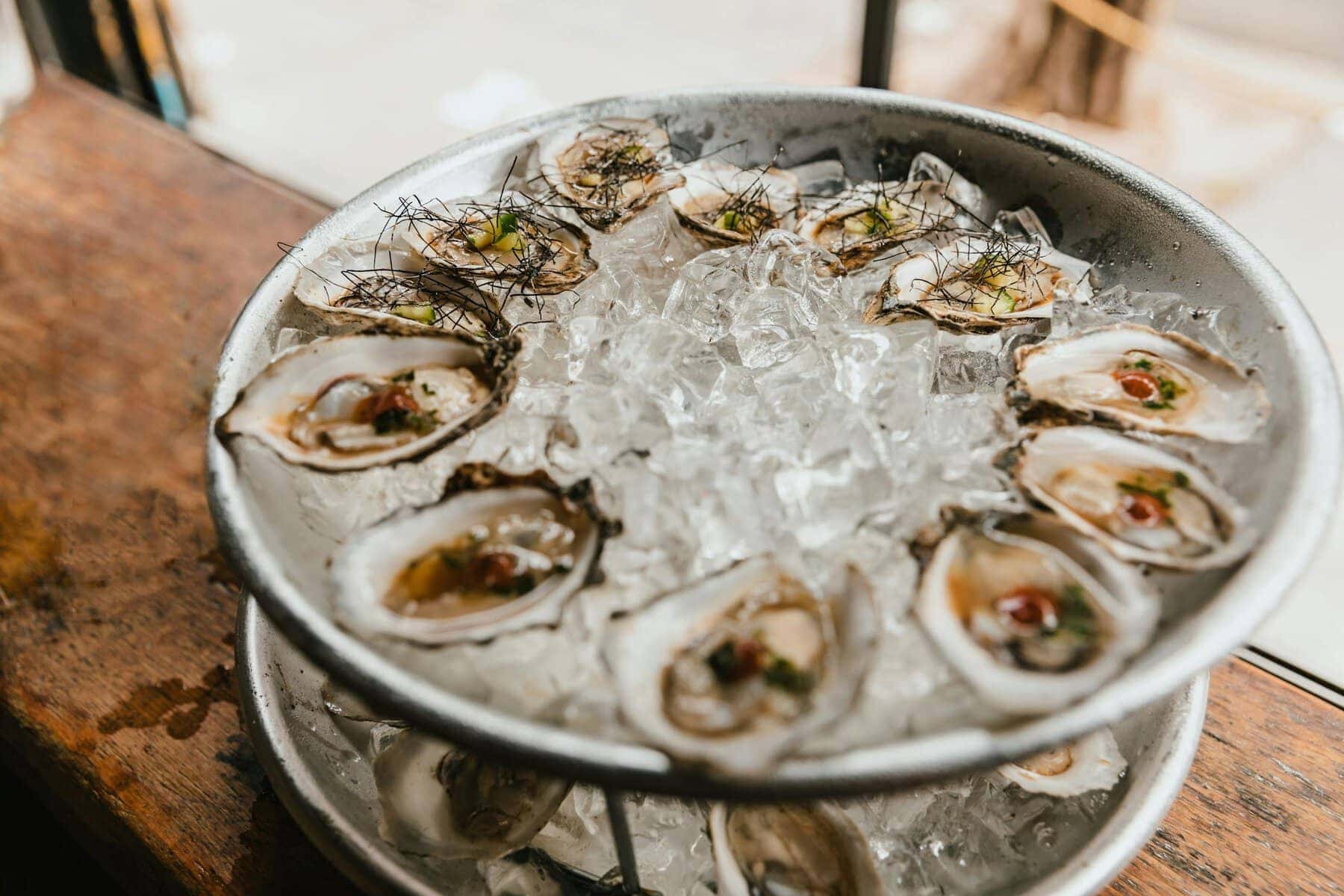 A delicious serving of oysters on ice, presented in metal bowls on a window sill.