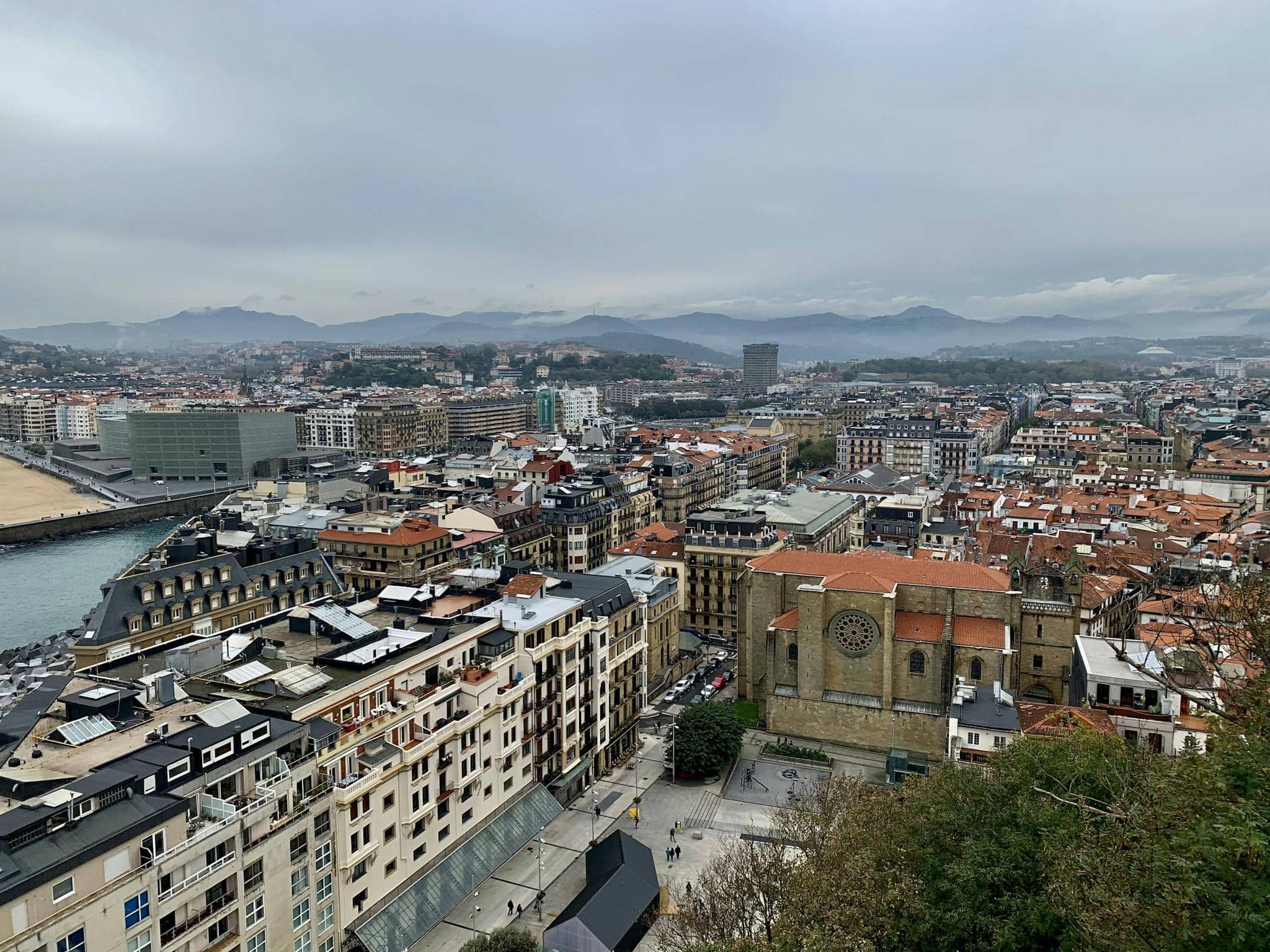Aerial view of San Sebastián, Spain with overcast skies and visible mountains.