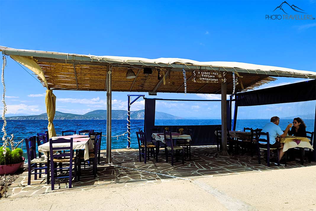 Direkt am Meer sitzen Menschen am überdachten Freisitz einer Taverne direkt am Wasser