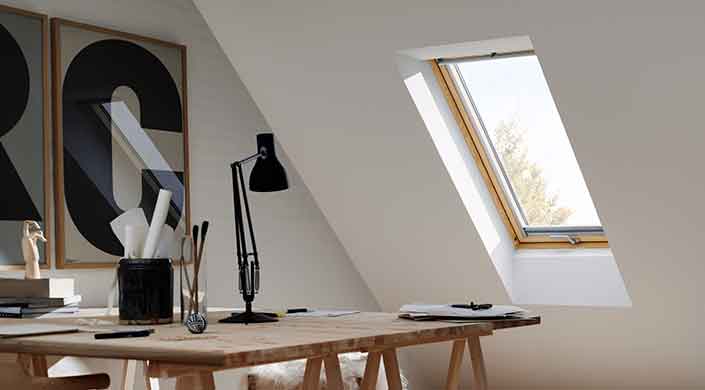 Holztisch unter einem Dachfenster in einem hellen Raum mit schräger Wand, einige Bücher und Pflanzen darauf, modernes, minimalistisches Design.