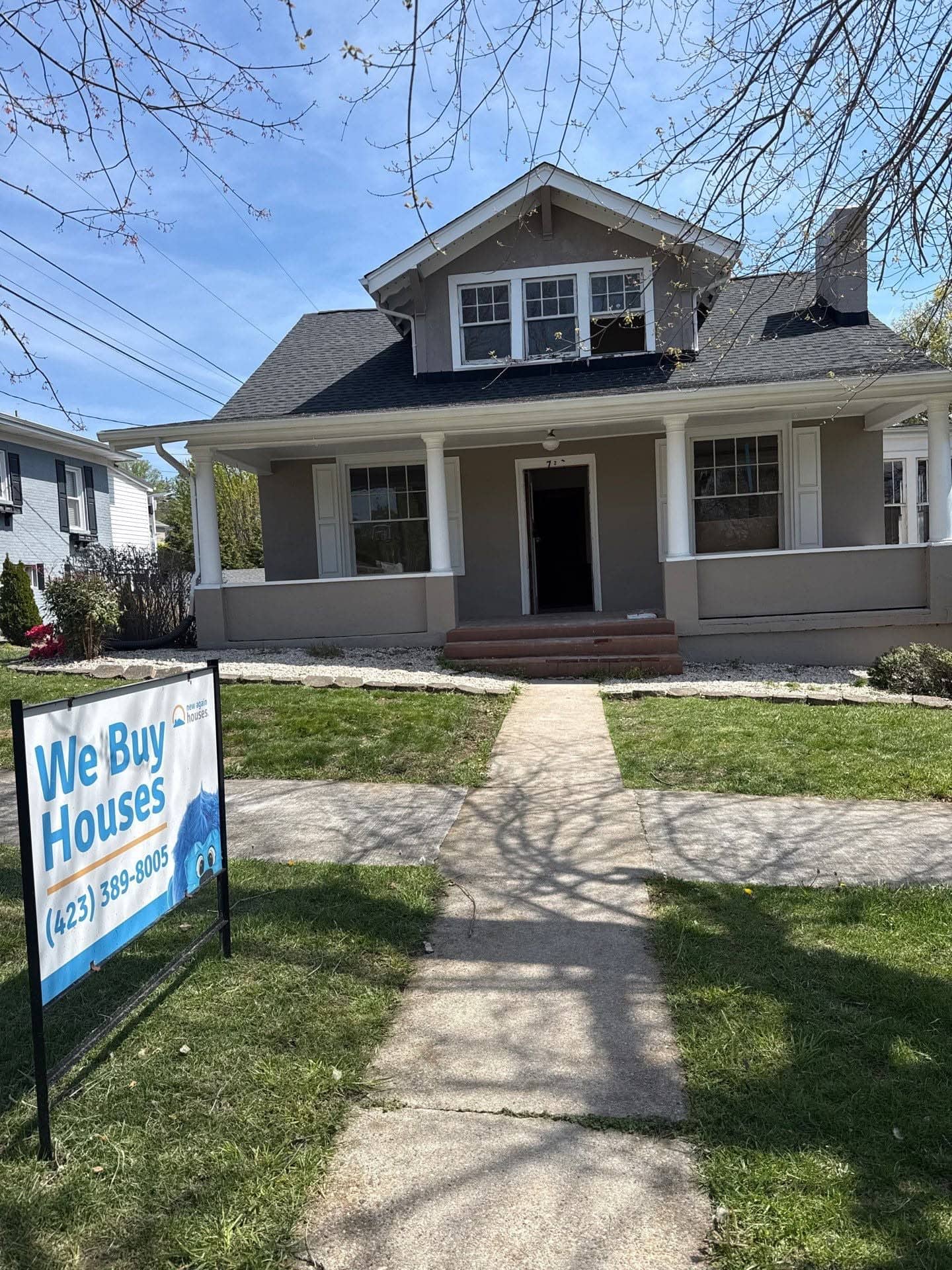 Tan craftsman-style house with a New Again Houses "We Buy Houses" sign in the front yard