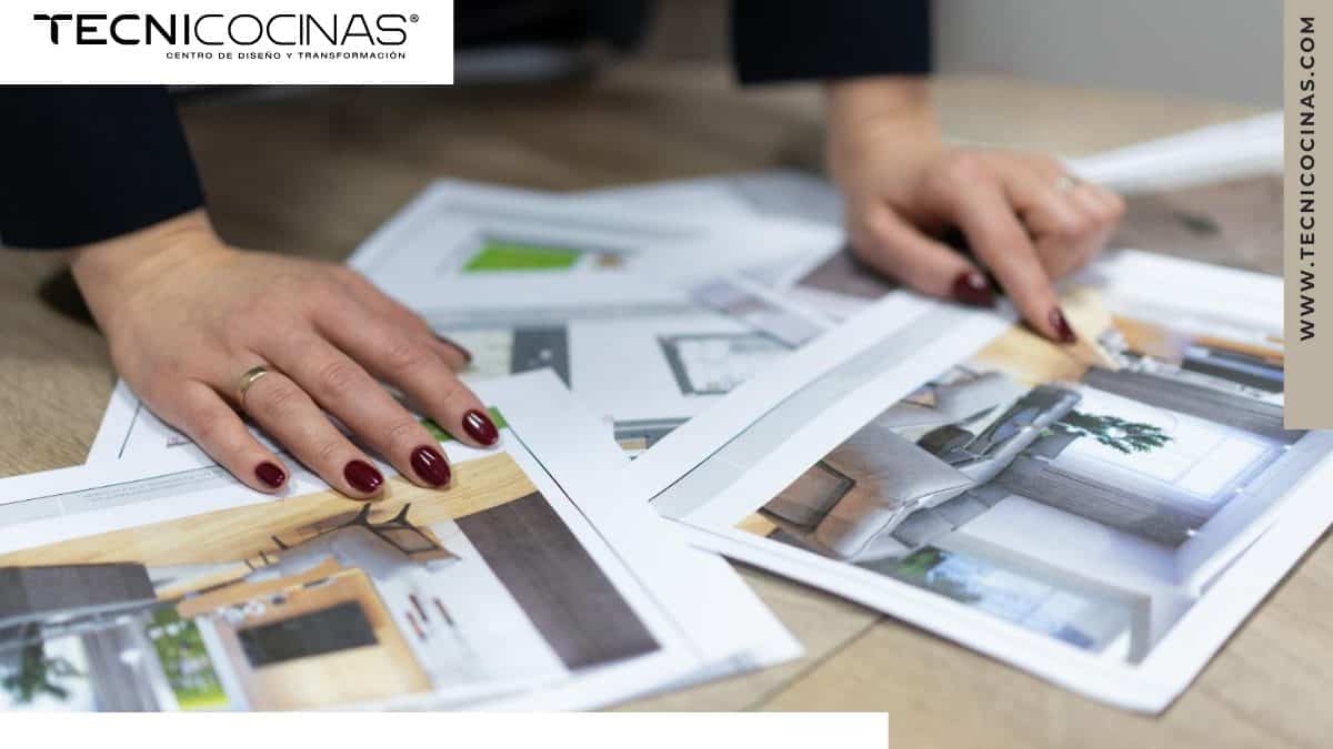 Persona observando imágenes de cocinas sobre una mesa, explorando diferentes estilos y diseños para inspirarse en la renovación de su cocina.