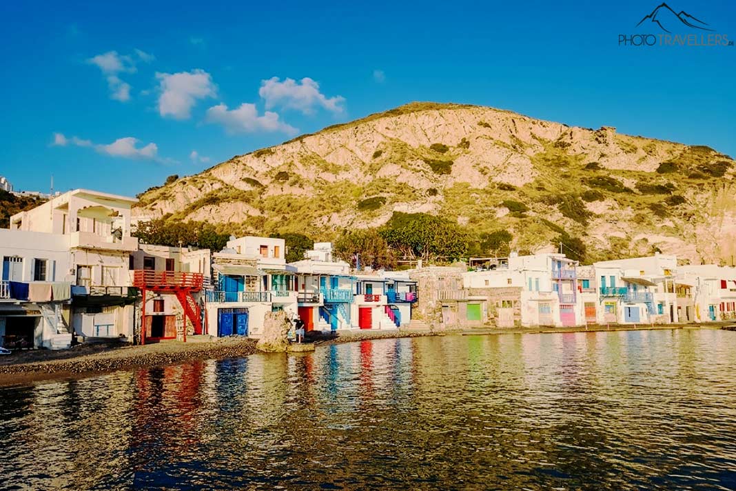Bunte Bootshäuser an der Küste von Klima mit Felsen im Hintergrund