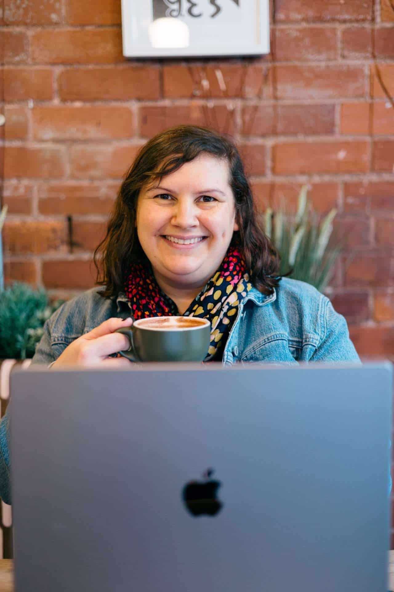 Lyndsey smiling with hot chocolate and laptop in Hereford cafe