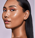 Seitliches Porträt einer Person mit glattem, schwarzem Haar und dezentem Make-up vor einem lila Hintergrund