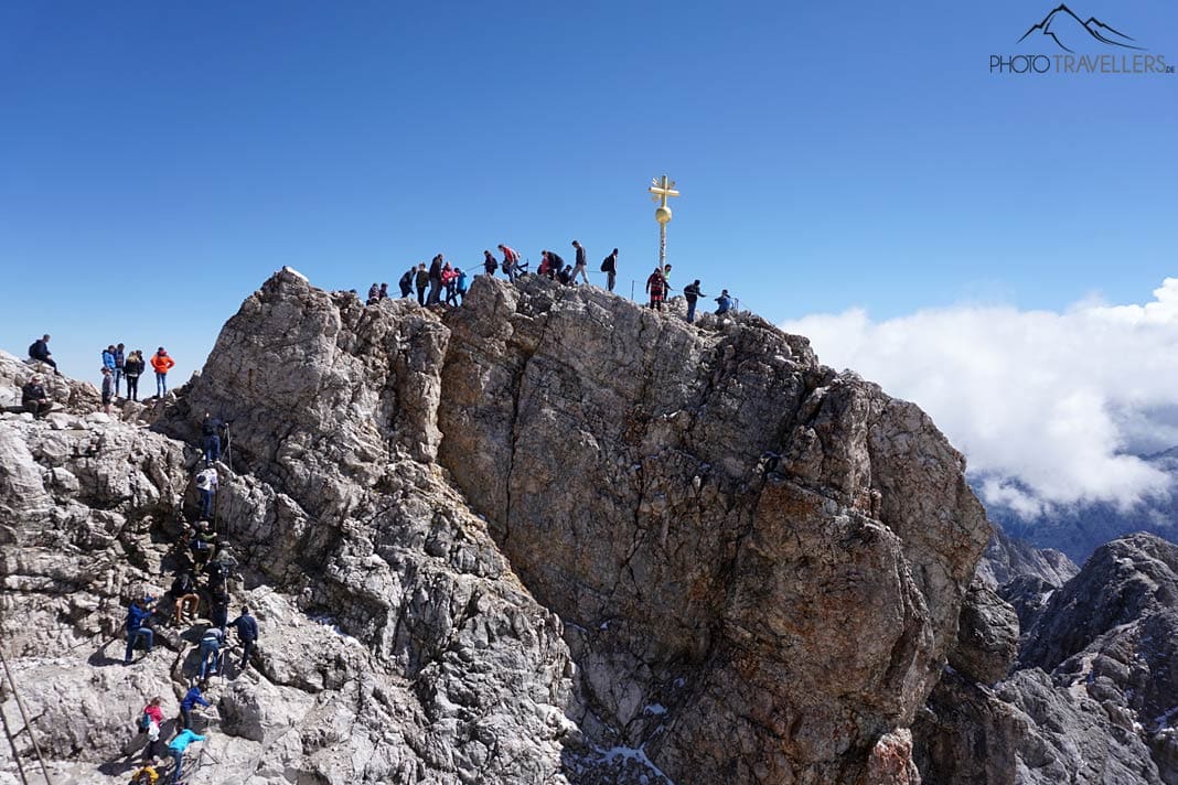 Menschen am Gipfel der Zugspitze mit dem goldenen Gipfelkreuz