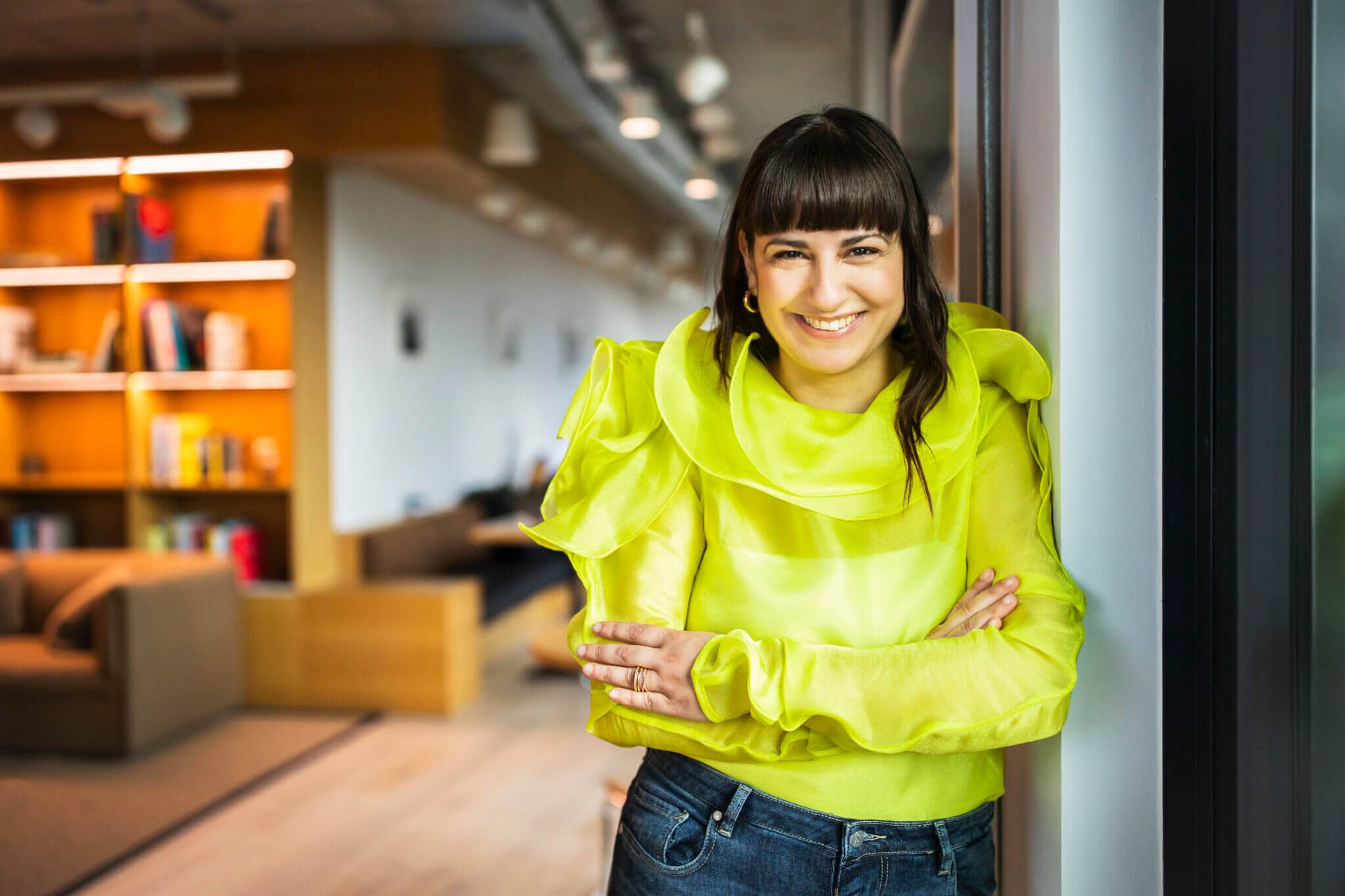 240621_Floria_Moghimi_0689-2 Floria Moghimi stands in a spacious office and beams at the camera. She is wearing a green and yellow blouse.