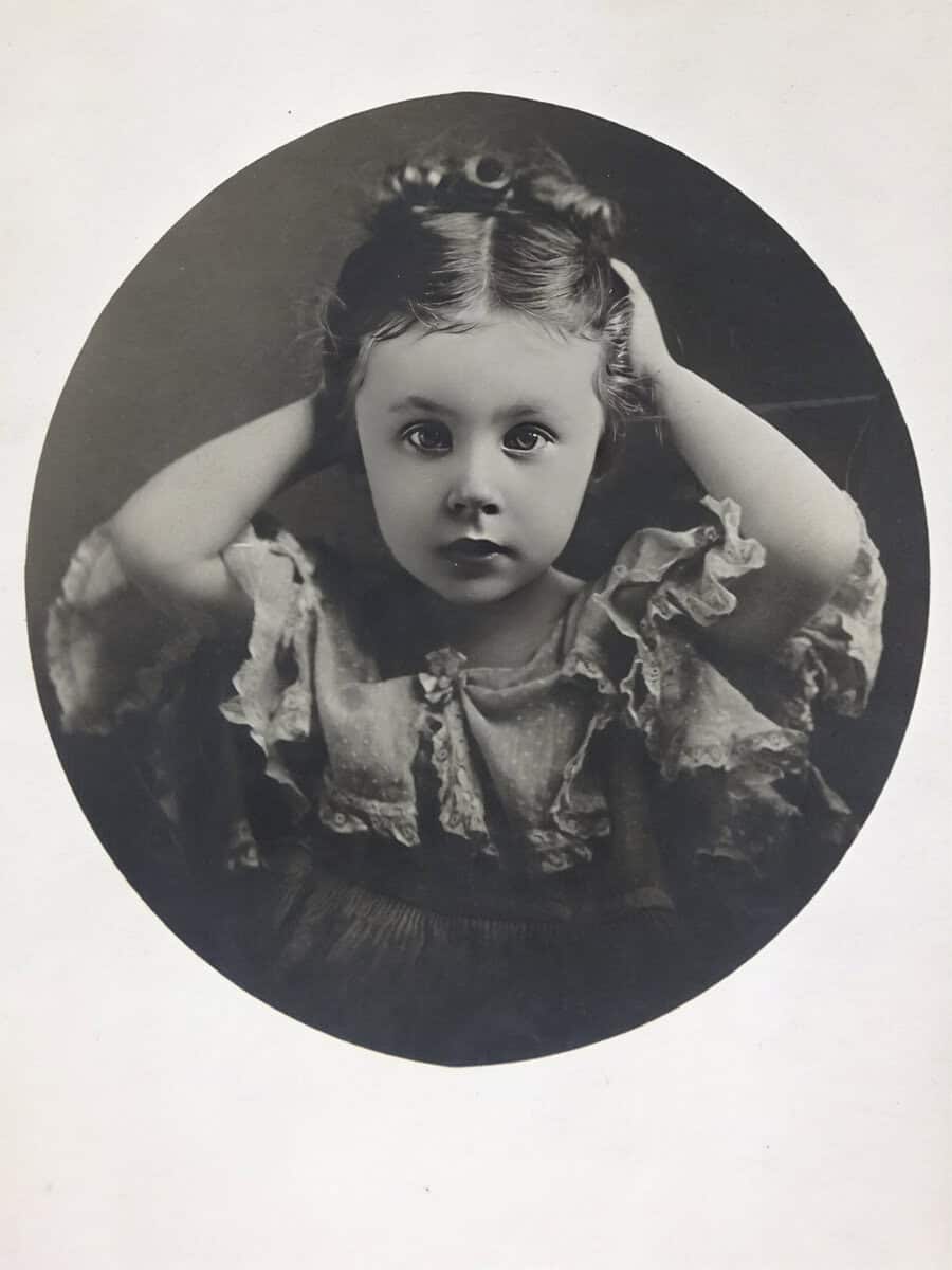 SC Oliver Child portrait, vintage black-and-white photograph, young girl with curly hair, expressive eyes, wearing ruffled dress, classic early 20th-century photography style at The History Museum.