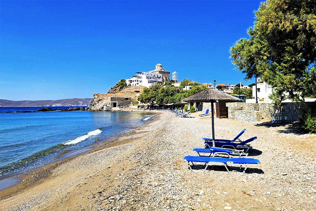 Wenige blaue Liegen mit Strohschirm am Sandstrand Kato Gialos mit dem Kloster im Hintergrund