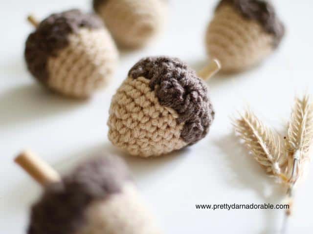 Close-up of crocheted acorns with brown tops, beige bottoms, and dried wheat on white. www.prettydarnadorable.com is visible. Free crochet pattern