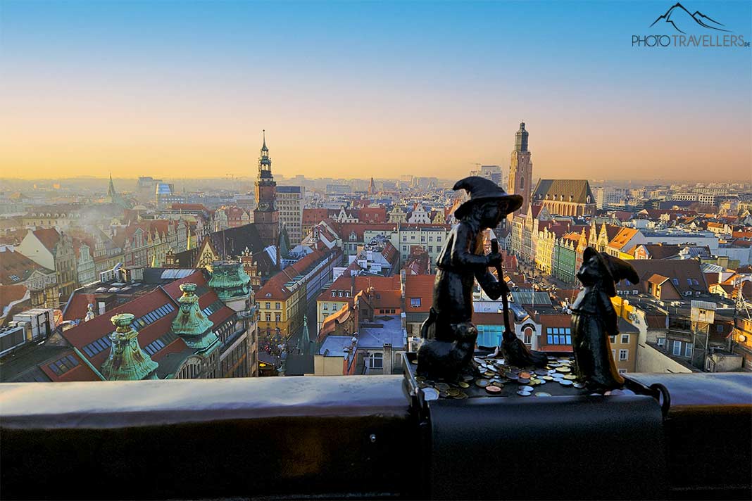 Zwei Zwergfiguren aus Metall sind auf einem Geländer hoch über der Stadtsilhouette von Breslau verankert