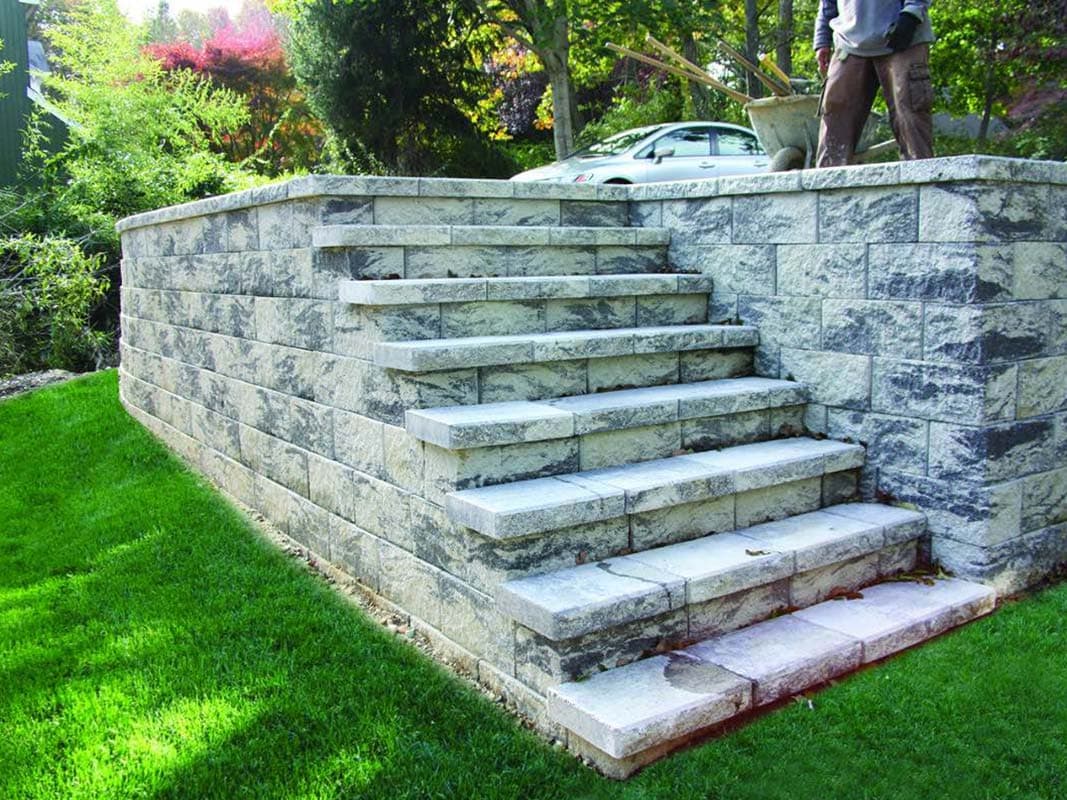 Stone steps leading up to a raised area with a man working on the upper level, next to a parked car in the background in Elwood.