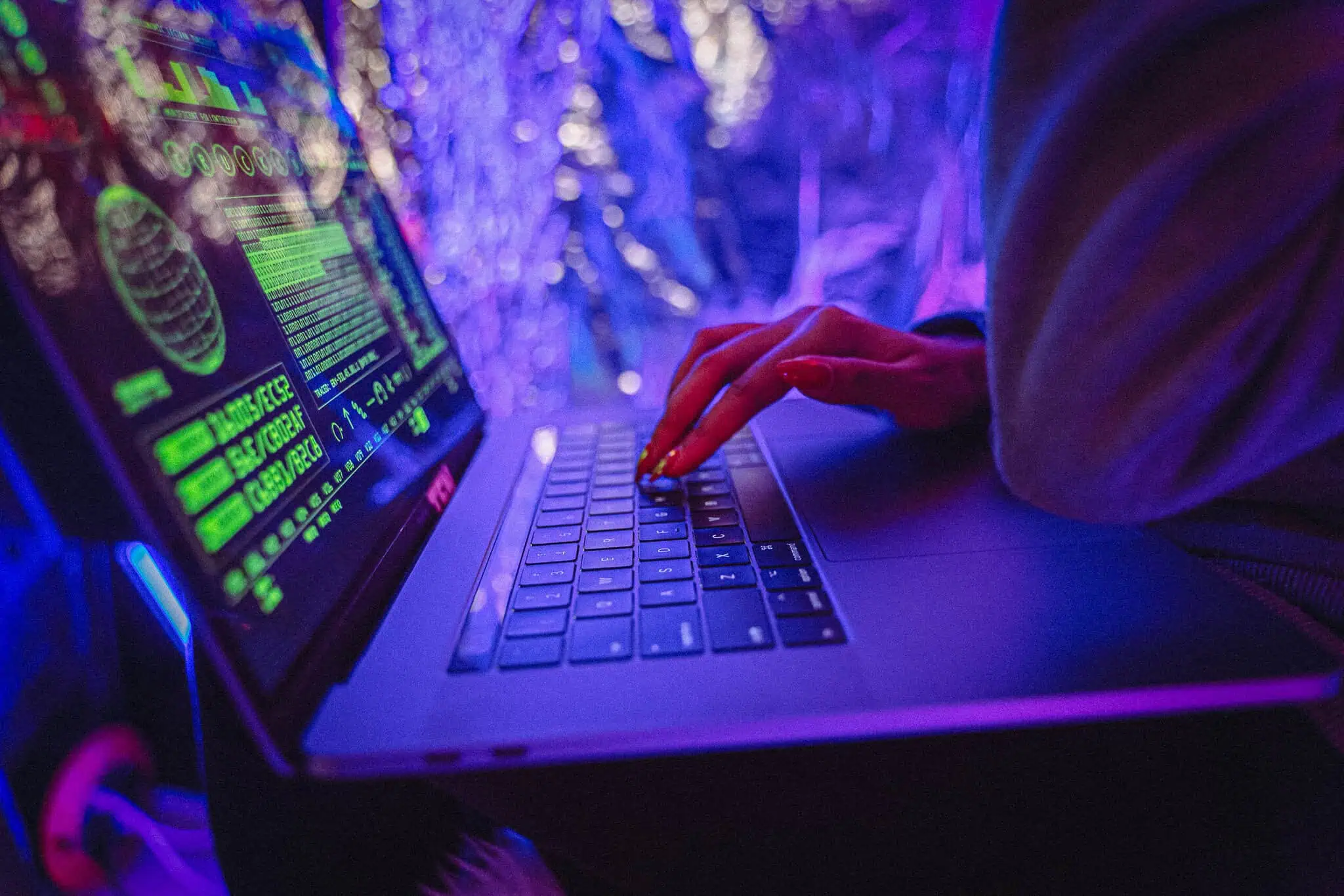 Person hacking on a laptop with dark web graphics and neon lights.