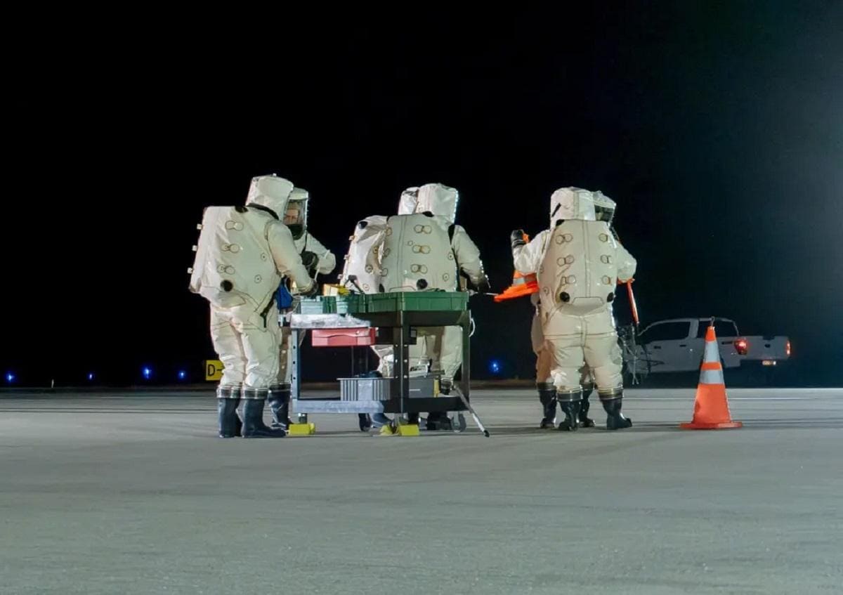 Hazmat-suited crews prepare for the X-37B landing, likely at Vandenberg Base, after a classified Space Force space mission. The unmanned spacecraft's return involves specialized protocols and ground crew operations.