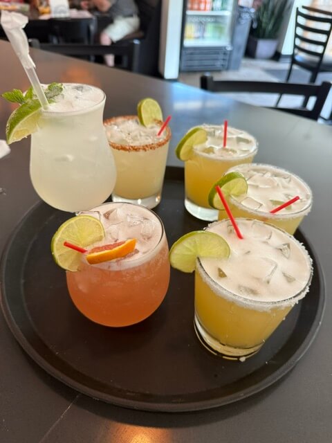 6 unique cocktails on a tray garnished with limes