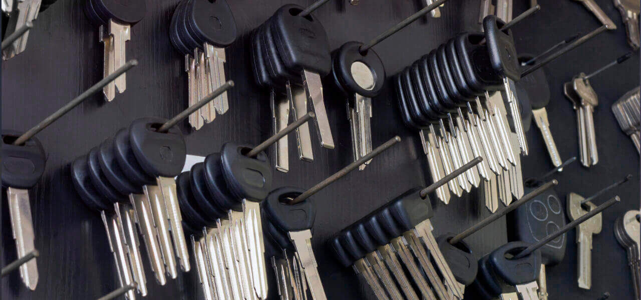 A wall-mounted board, reminiscent of a locksmith’s workspace, showcases numerous sets of keys organized on hooks. Each set, featuring black plastic heads, is arranged in rows depicting various types. Some keys have distinct shapes for different locks, with a few individual ones scattered around.