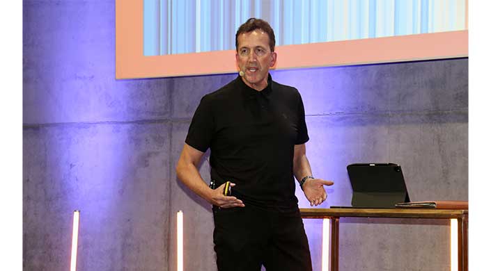 Bild von Karl-Heinz Krawczyk als Keynote-Speaker Ein Mann in schwarzem Hemd spricht auf einer Bühne und trägt ein Headset-Mikrofon.