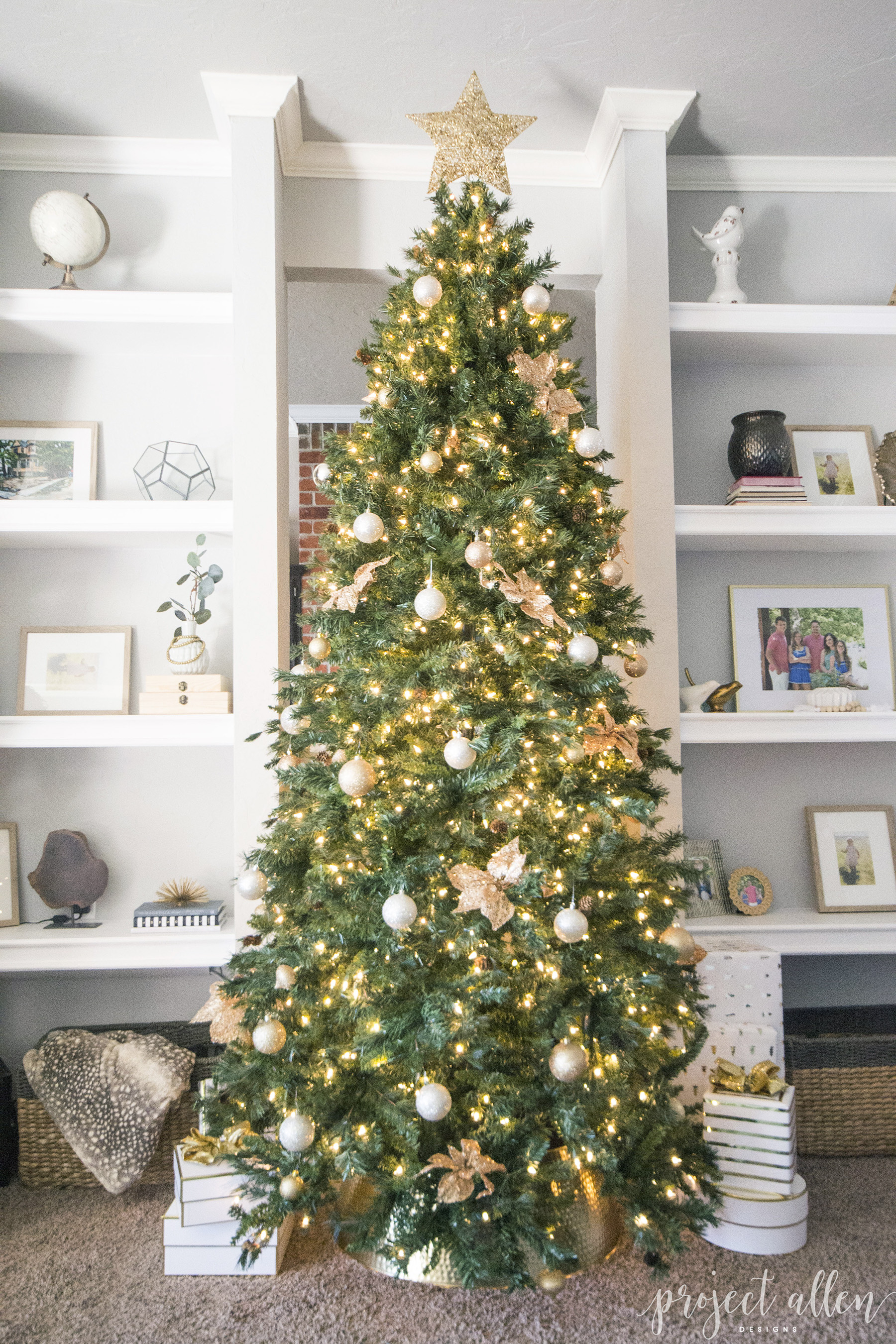 Modern Glam Christmas tree with gold ornaments, brass tree collar, glittered magnolia leaves and white and gold Christmas gifts tadd the perfect touch to these custom built-ins.