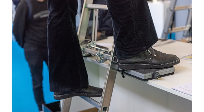 Eine Person steigt eine silberne Metallleiter hinauf, nur die Beine und Schuhe sind sichtbar.