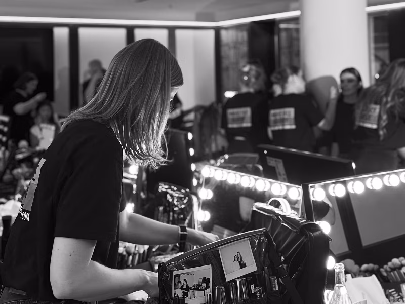 Person mit Famous Face Academy T-Shirt vor einem Schminkspiegel
