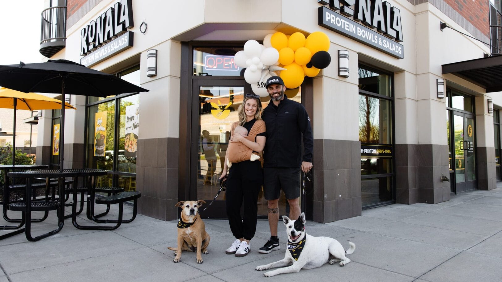 Trace and Jammie Miller celebrate a Konala grand opening with their newborn and rescue dogs Kona and Nala, the very two dogs the brand is named after. Image Courtesy of Konala