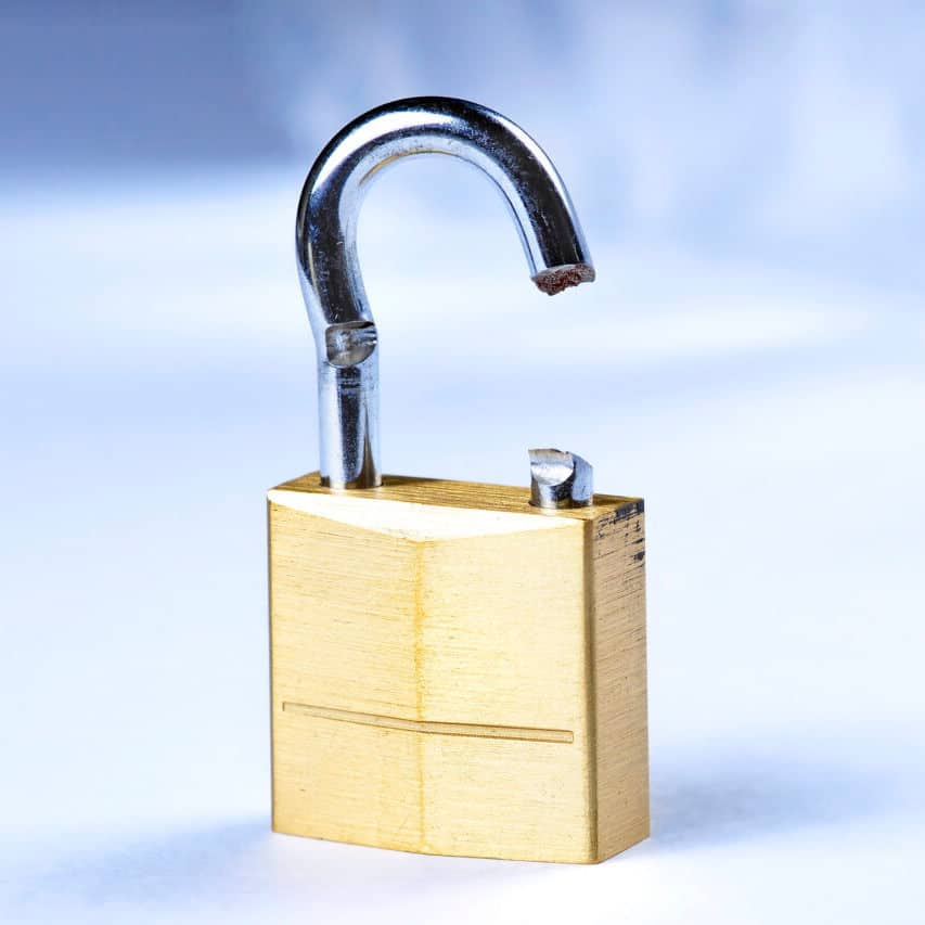 A close-up image of a broken padlock. The padlock, clearly illustrating why a skilled locksmith is essential, is made of brass with a silver shackle, which is bent and snapped on one side, rendering it non-functional. The background is out of focus, making the padlock the focal point of the image.