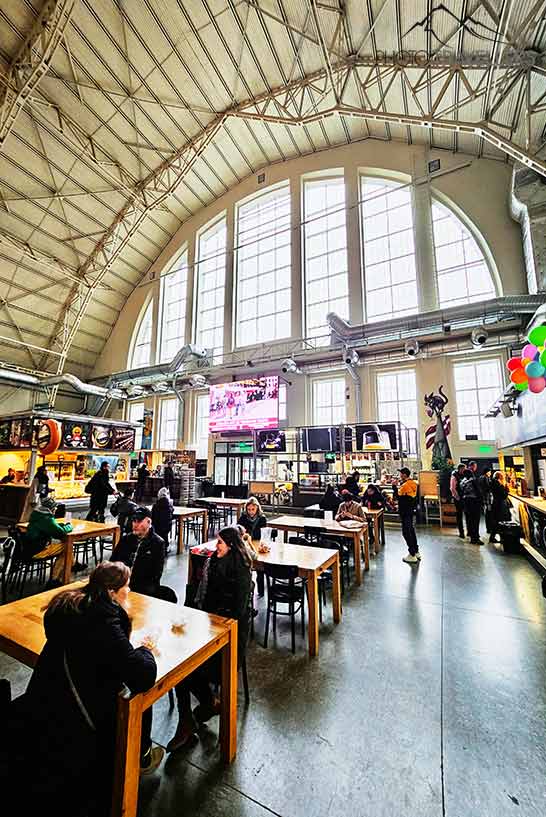 Viele Tische mit Gästen stehen in der hohen Markthalle von Riga