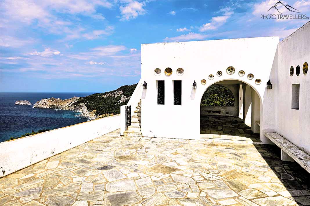 Flache weiße Fassade mit gepflasterter Terrasse der Kapelle Agios Alexandros über dem Meer