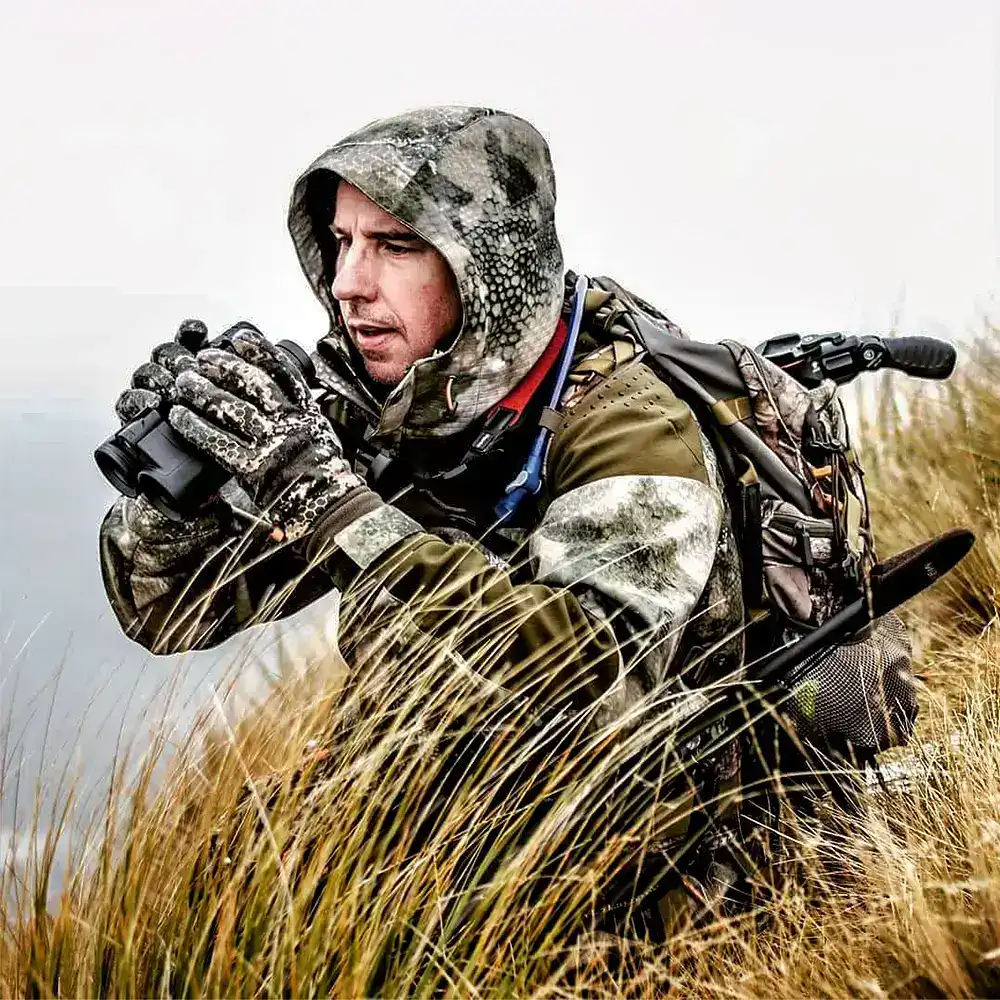 Jagdreise Neuseeland – Bergjagd & Beobachtung mit JAGD TOTAL Jäger in Tarnkleidung beobachtet mit Fernglas das Gelände in den Bergen – Jagdreise nach Neuseeland mit JAGD TOTAL