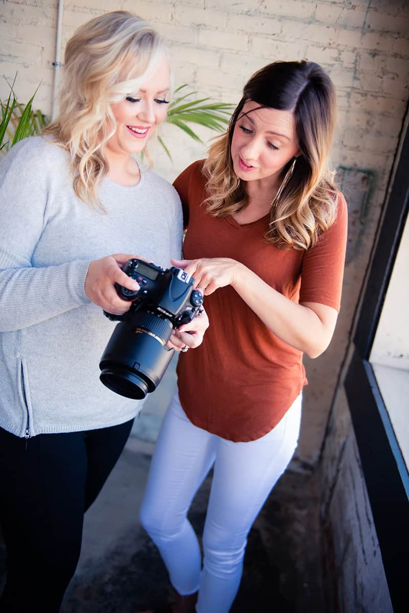 Two women at a marketing agency review photos on a professional camera together.