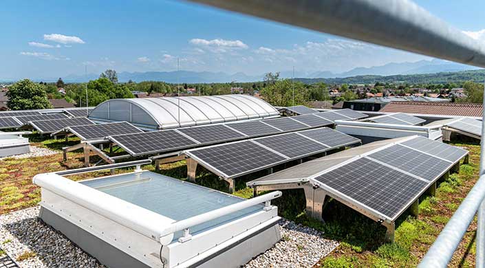 Solarmodule auf einem Gebäudedach mit grünem Hintergrund und blauem Himmel.