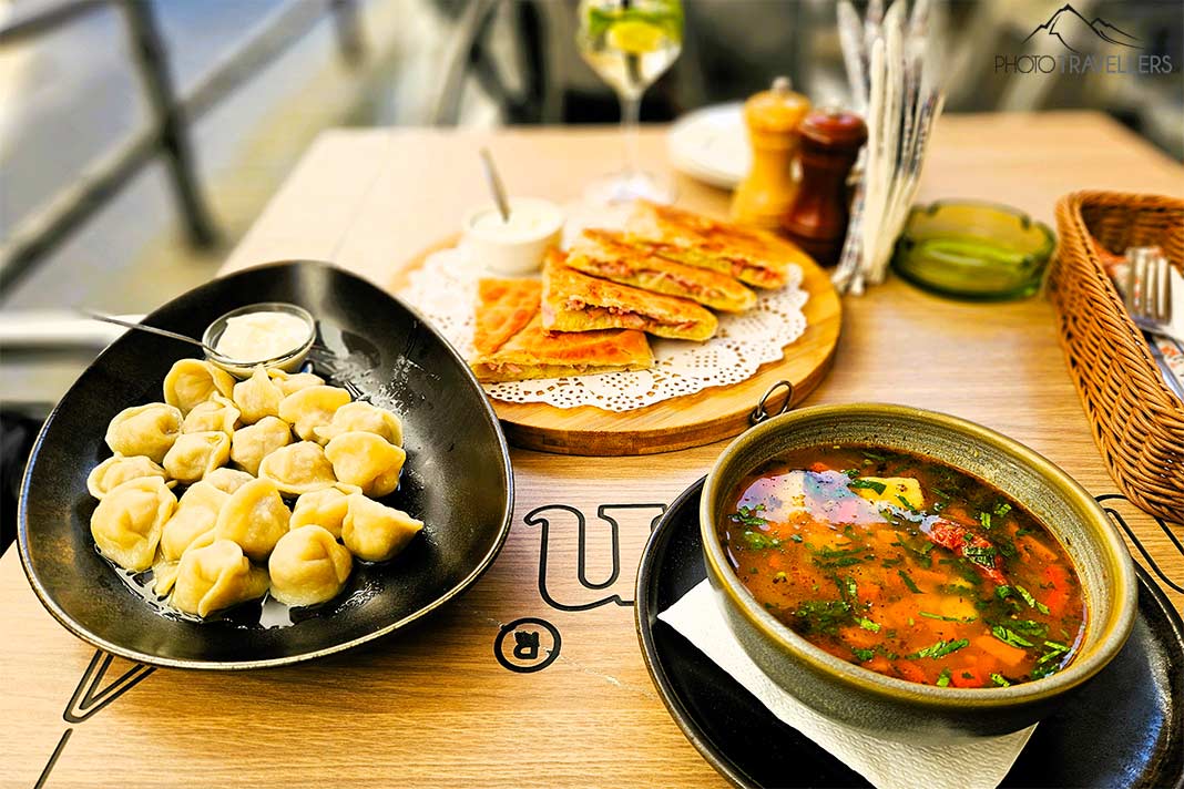Drei Teller gefüllt mit Fladenbrot, Suppe und Pelmeni stehen auf einem Tisch